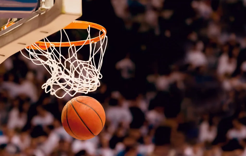 Ein Basketball faellt durch das Korbnetz vor verschwommenem Hintergrund