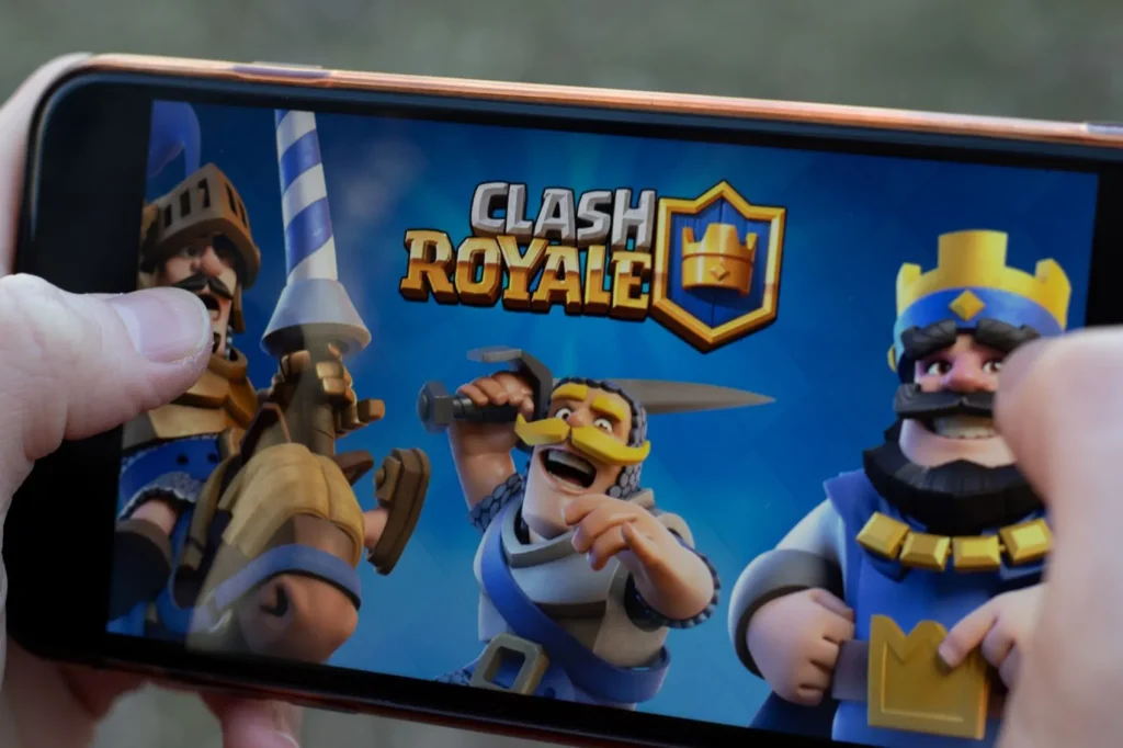 Smartphone mit Clash Royale Logo und Bildern in den Händen eines Kindes